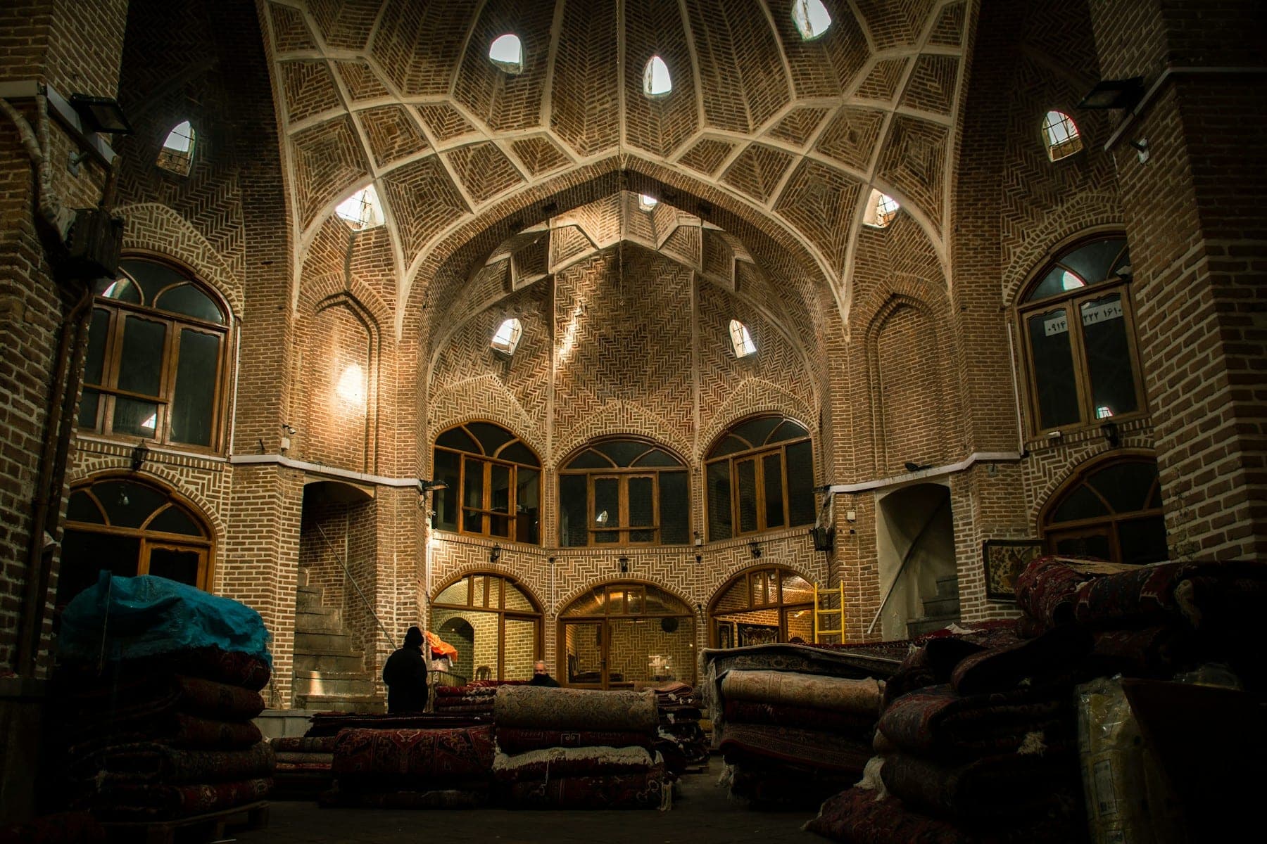 Domed brick caravanserai with bales and piles of carpets beneath skylights
