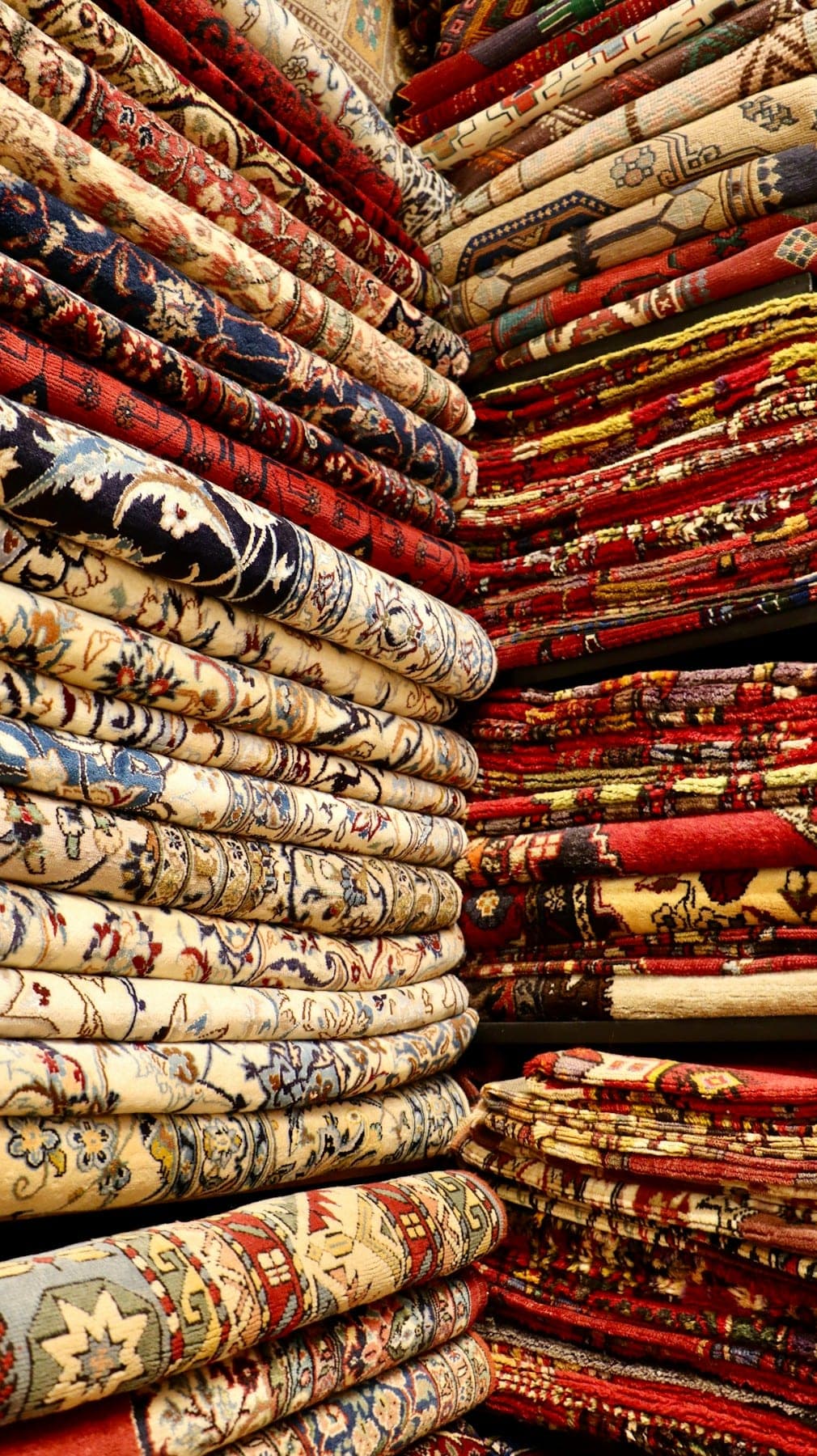 Floor-to-ceiling stacks of folded rugs in a bazaar shop