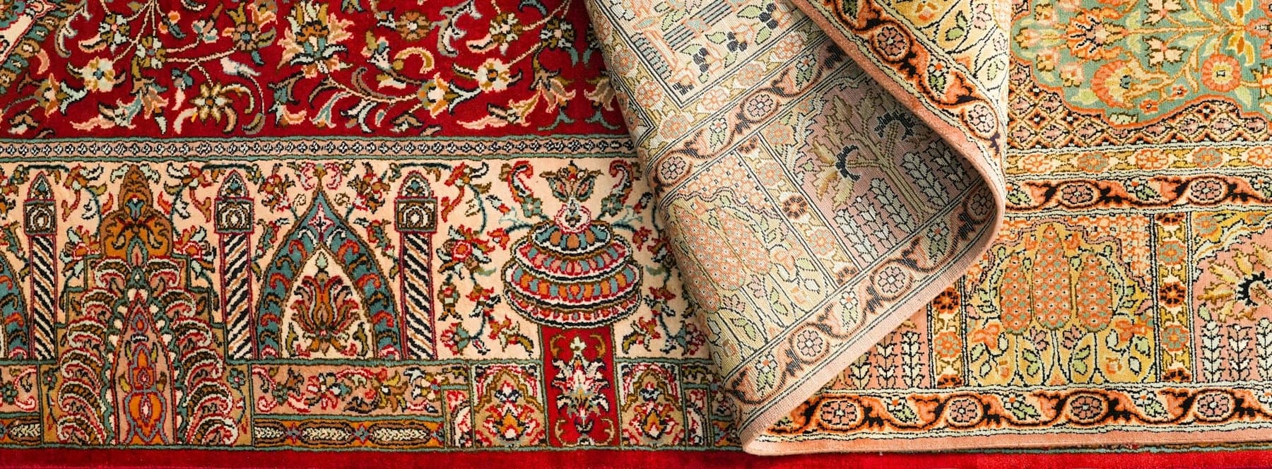 Two finely knotted silk rugs, one folded back, in crimson and gold