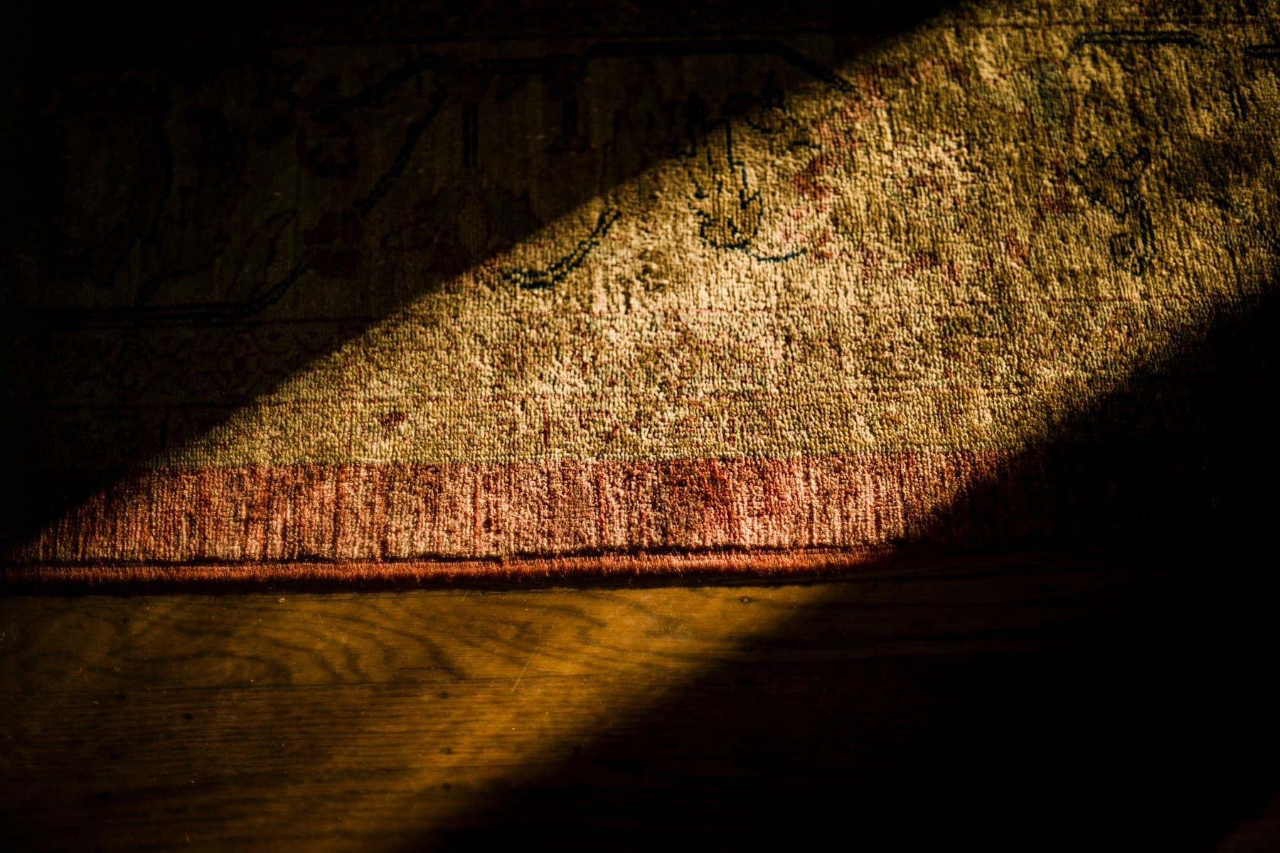 A shaft of light across a worn rug edge on dark floorboards