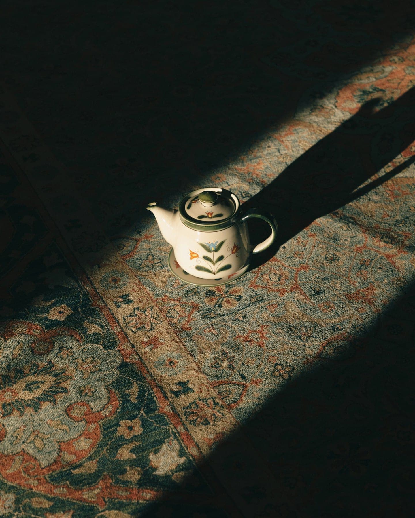 Painted teapot on a faded rug in a slant of late sun