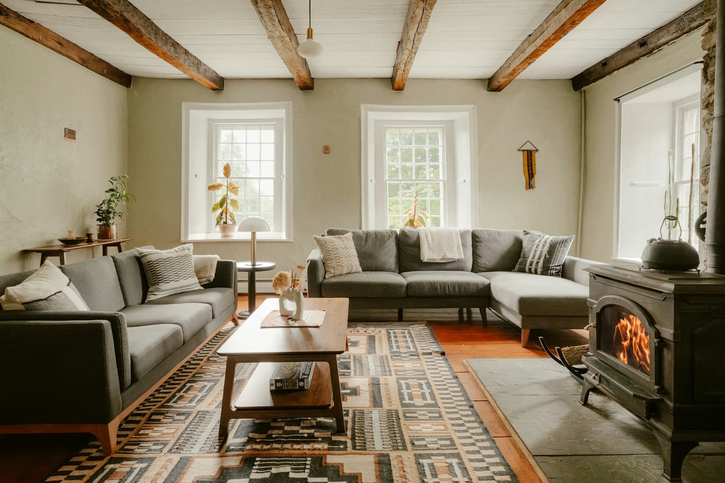Beamed farmhouse living room with grey sofas, a wood stove and a geometric kilim runner