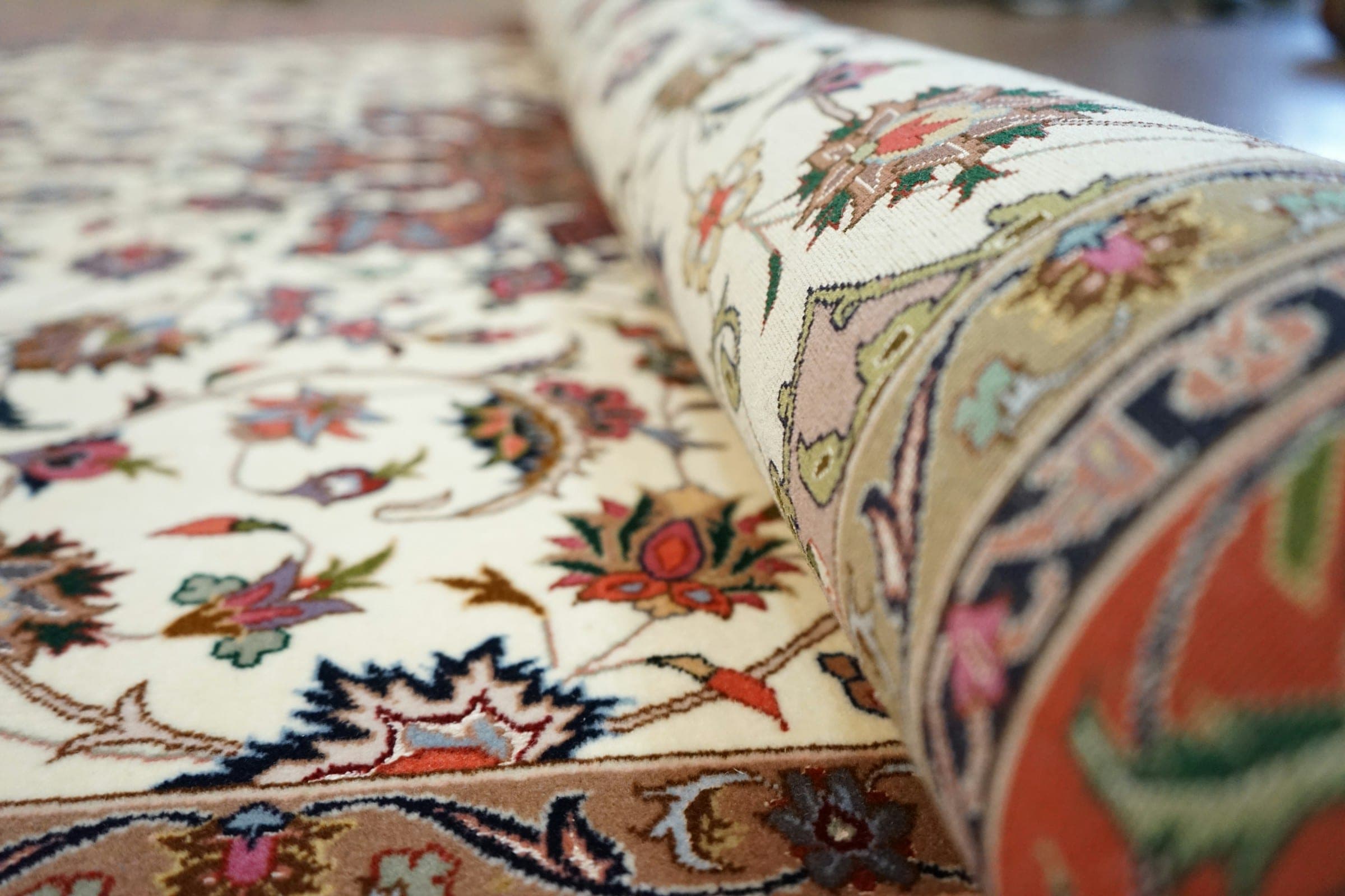 Close view of an ivory floral hand-knotted rug being unrolled