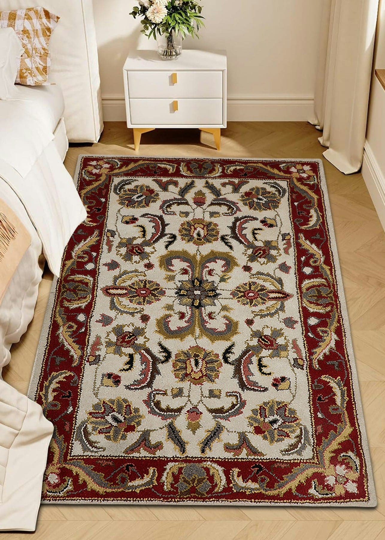 Ivory and crimson floral rug beside a bed on herringbone parquet