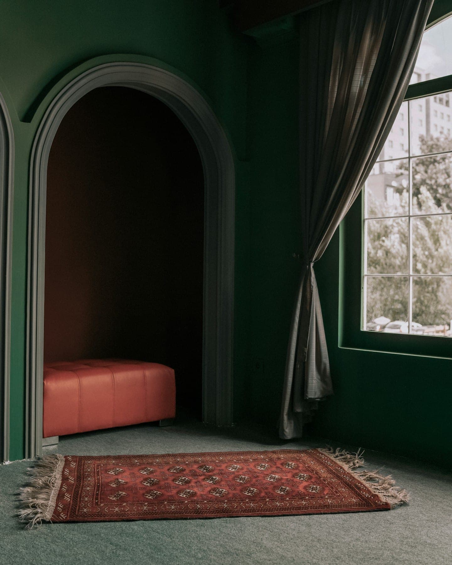 Deep green arched alcove with a small red Bokhara rug and a linen curtain