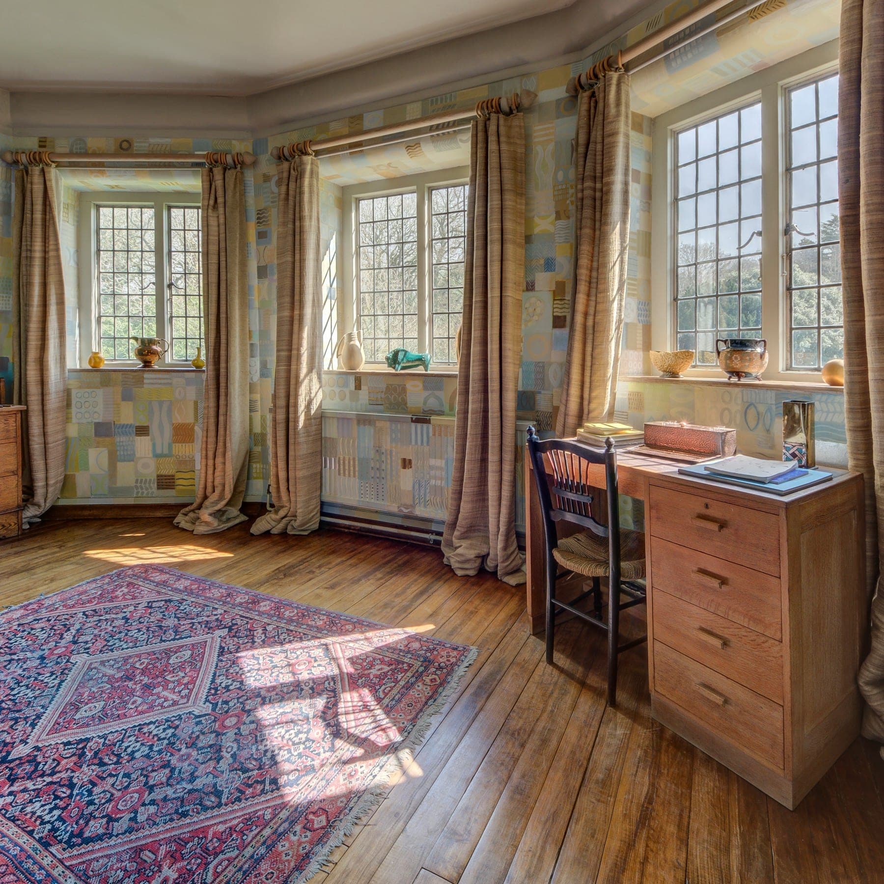 Sunlit study with leaded bay windows, an oak desk and a faded blue-red Persian rug
