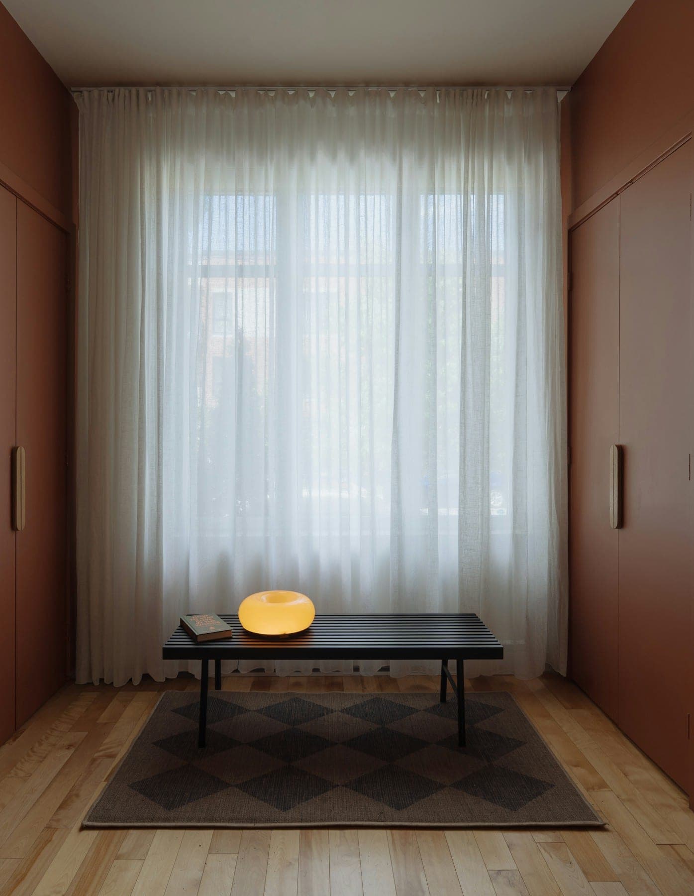 Minimal terracotta room with sheer curtains, a low table and a checked wool rug