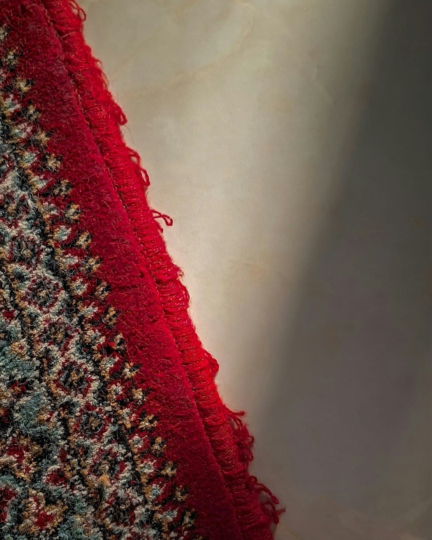 Crimson overcast edge of a fine rug curving against a pale wall
