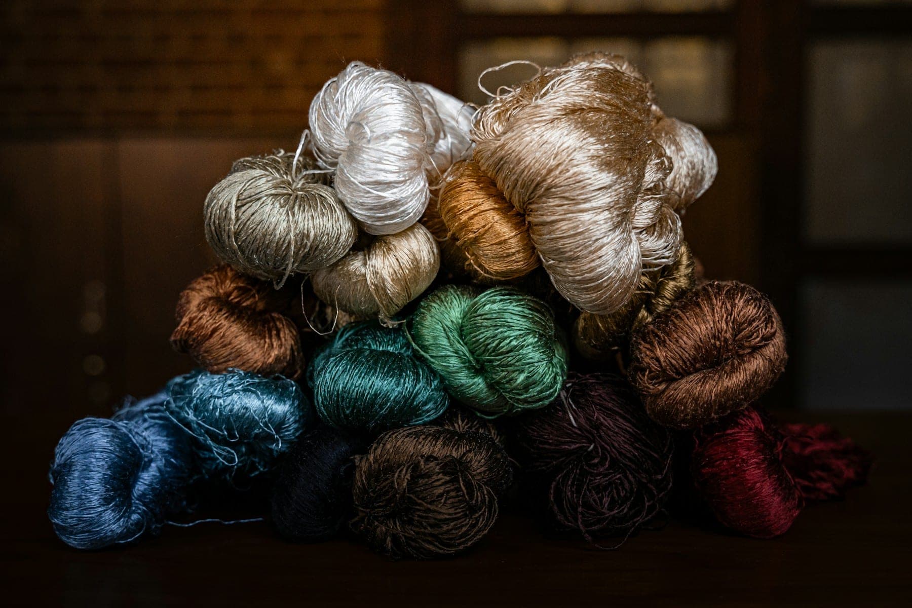 Pile of lustrous silk skeins in ivory, jade and indigo on a dark table