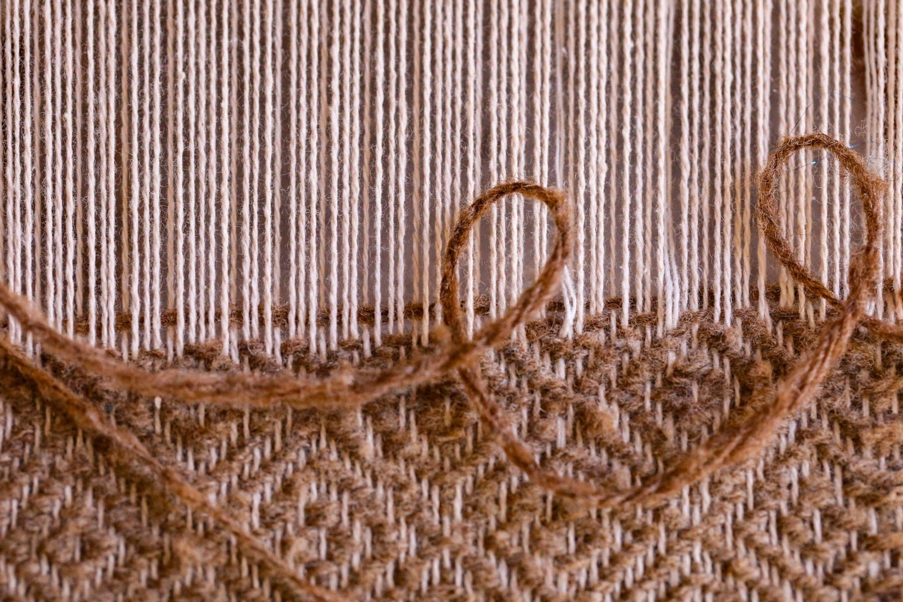 Undyed warp threads and loose wool weft above a partly woven panel