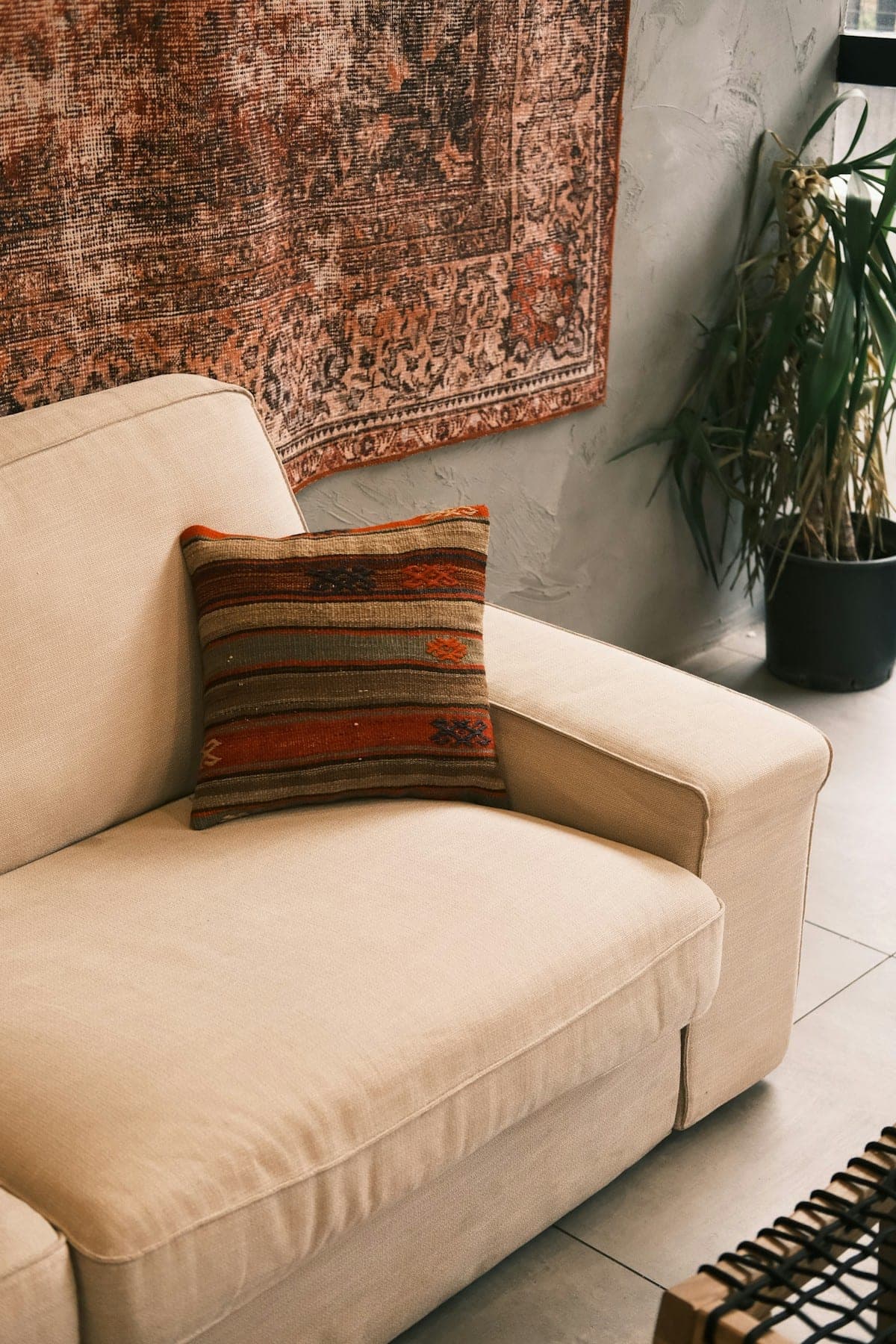 Cream sofa with a kilim cushion beneath a faded vintage rug hung on the wall